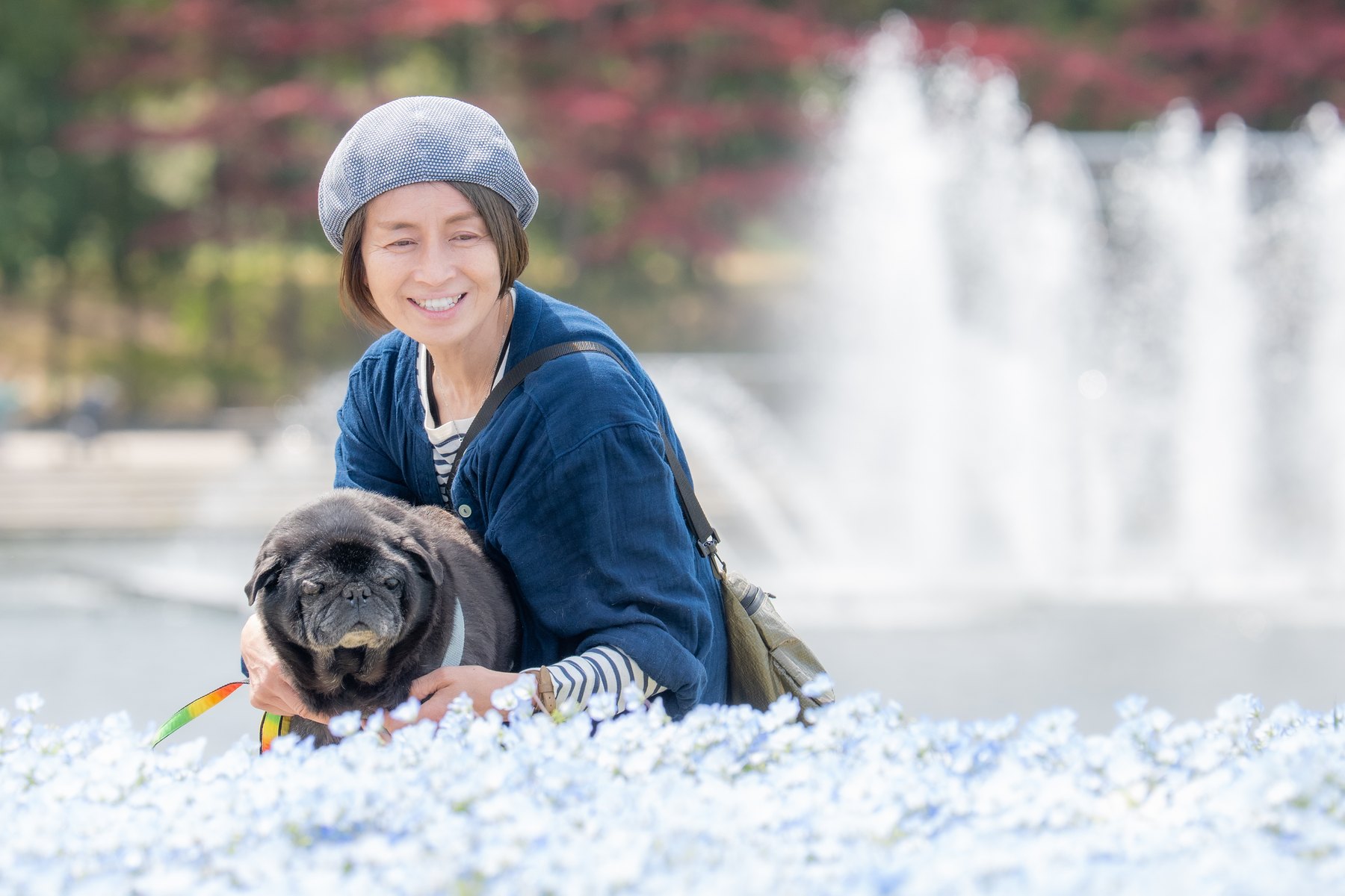 花の中で黒い小型犬を抱く女性